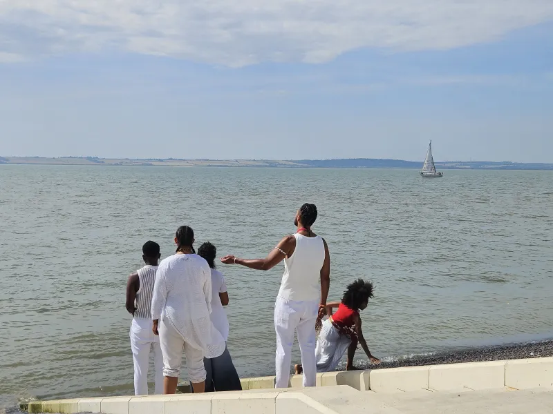 Choir singing in front of the Thames Estuary with a boat sailing in the distance