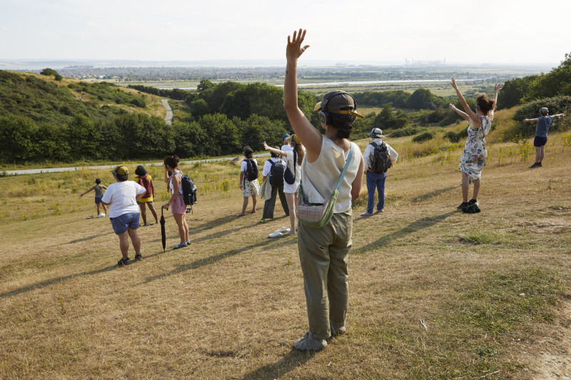 A group of people with arms in the air on a hill facing the Estuary wearing headphones